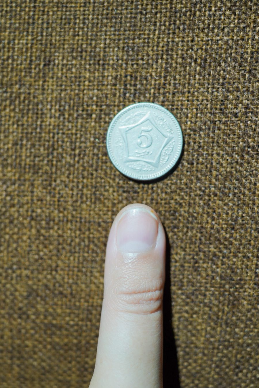 Thumb extended flat with coin placed above the thumbnail — the canonical thumb photo for sizing