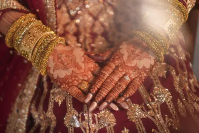 Caramel cat-eye almond press-on nails on hands with mehndi over a maroon bridal outfit