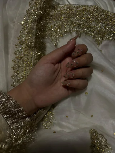Almond nude press-on nails with gold beads resting on a white and gold bridal outfit